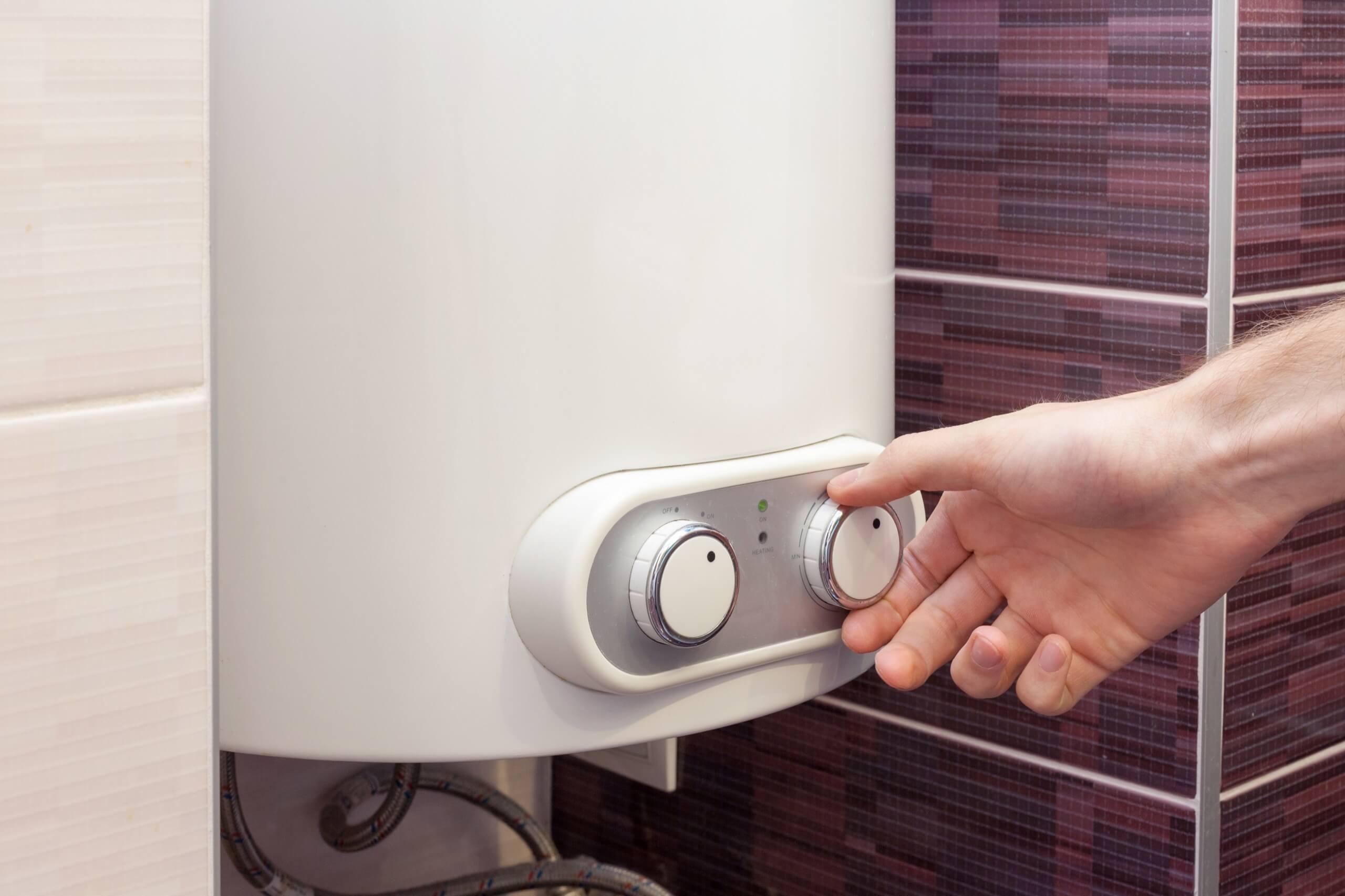 A man's hand adjusts the temperature setting on an electric water heater.