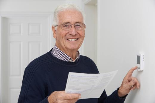 A man adjusting his thermostat and smiling because of the energy he is now saving