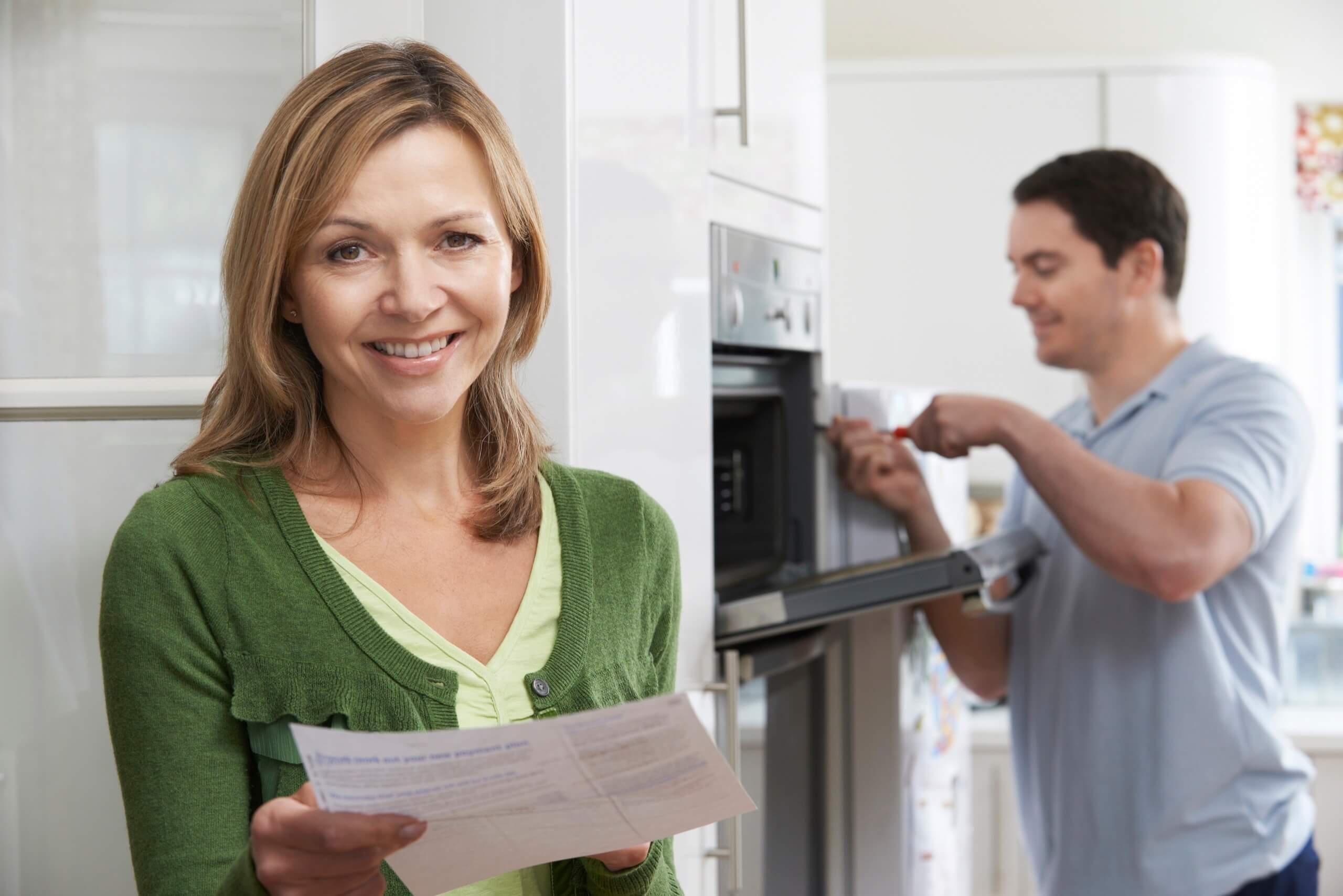 Couple sits in kitchen while hushband works on repairing their stove