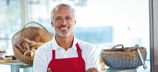 Man in red apron smiling in bakery