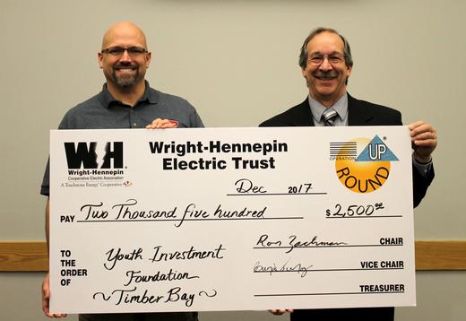 Two people hold up check given to them by Wright-Hennepin Electric