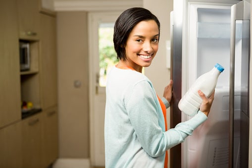 Woman holding a bottle of milk in front of the fridge