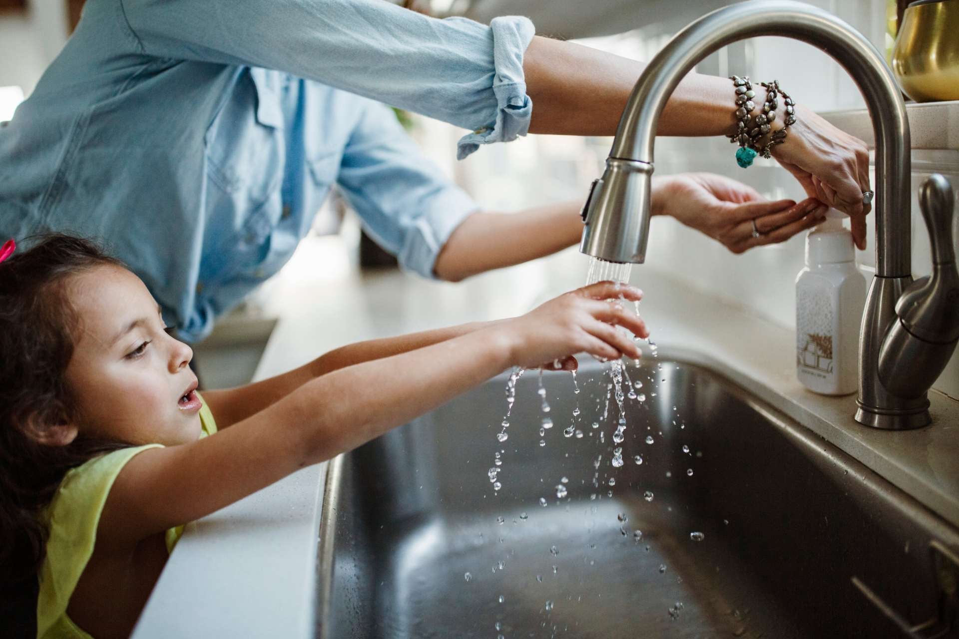 Kid reaching up to wash hands in kitchen sink