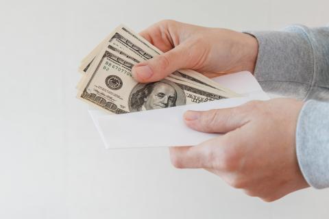 a hand pulls several hundred dollar bills out of an envelope